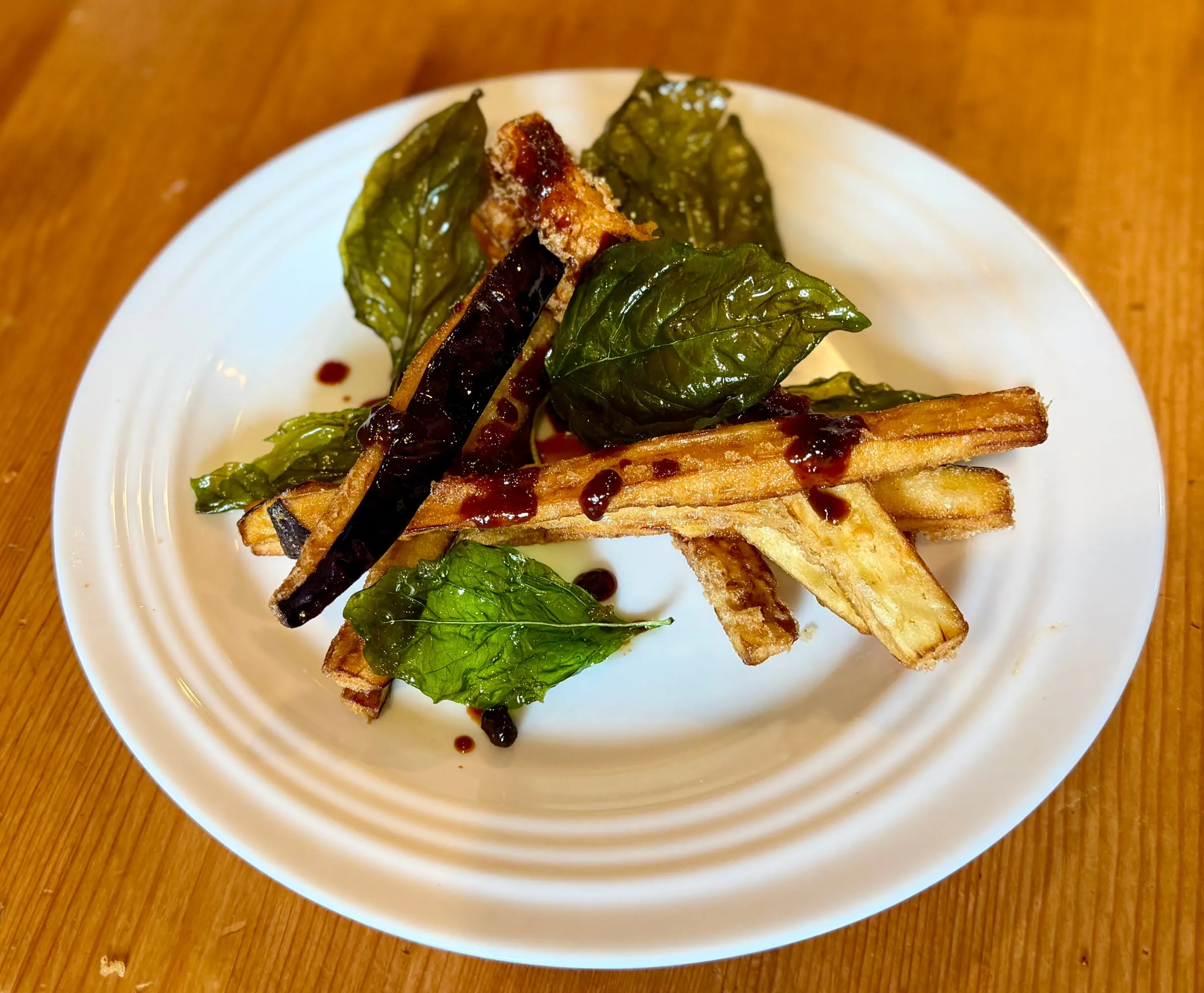 The same fried eggplant and crisp basil dish from a lower angle, the glaze pooling on the eggplant skin.